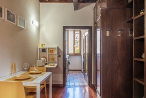 A narrow hallway with a dining area on one side, a wooden cabinet on the other, and a door leading to an outdoor area.