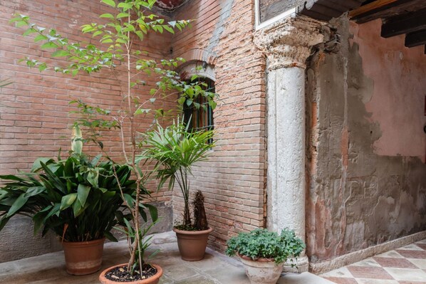A courtyard with potted plants, a brick wall, and a column.