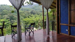 A wooden deck with two chairs and a table, overlooking a lush green forest. - Ecohotel SoñArte (Córdoba)