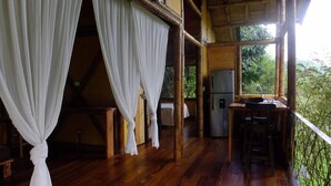 Una cabaña de madera con balcón, refrigerador y una mesa con sillas.