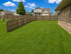 A residential backyard with a wooden fence, a well-maintained lawn, and houses in the background. - Geographical Oddity: Close to Everything! / Fiber Internet / EV Charger! (Huntsville)