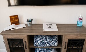 A wooden desk with a sign, a guest book, a pen holder, a booklet, and a bottle of hand sanitizer. - Geographical Oddity: Close to Everything! / Fiber Internet / EV Charger! (Huntsville)