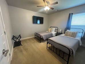 A bedroom with two beds, a ceiling fan, a TV, and a window with blinds.