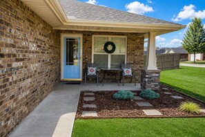 A brick house with a blue door, a covered porch, a stone pillar, and a wreath on the window.