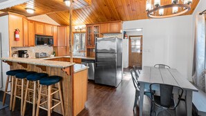 A modern kitchen with wooden cabinets, stainless steel appliances, a bar area with stools, and a dining table with chairs.