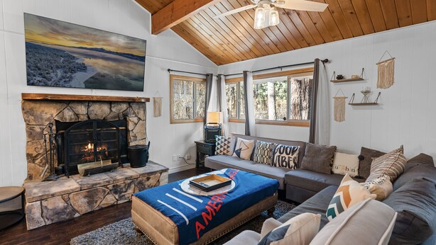 A cozy living room with a stone fireplace, a large painting, and a ceiling fan.