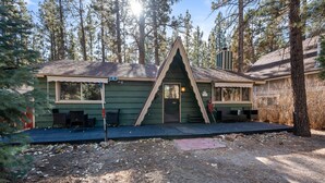 A cabin with a triangular roof, a porch with chairs, and a deck area.