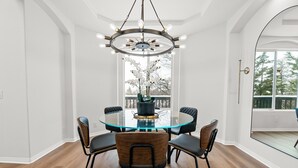 A modern dining room with a glass table, four chairs, and a central chandelier.