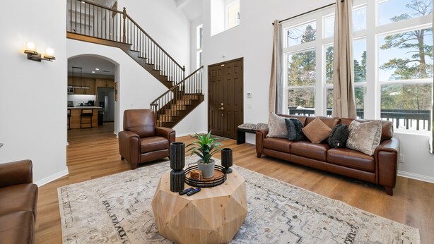 A spacious living room with a wooden coffee table, leather sofas, and a staircase leading to the upper floor.