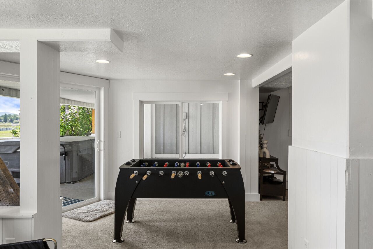 A foosball table in a room with white walls and a door leading to a balcony.