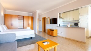 Ein modernes Hotelzimmer mit Bett, Sofa, kleinem Tisch, einer Küchenzeile und einem Fernseher.