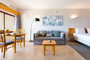 A modern hotel room with a dining area, a gray sofa, a small table, and a bed.
