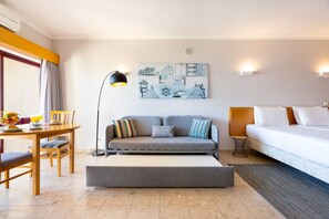 A modern hotel room with a sofa, a bed, a dining table with chairs, and a painting on the wall.