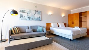 Ein modernes Hotelzimmer mit einer Couch, einem Bett, einem Nachttisch und einem Wandbild.