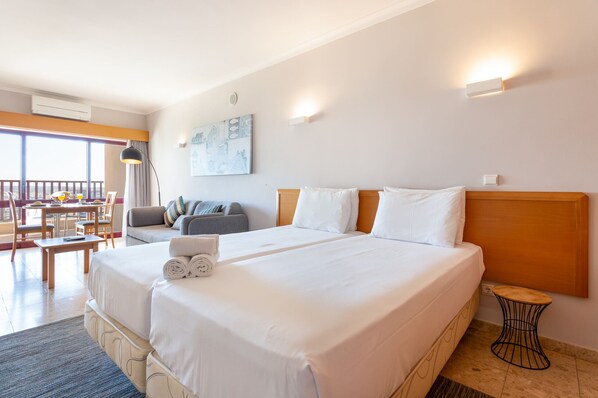 Habitación de hotel con una cama grande, una mesita, un sofá y un balcón con mesa y sillas.