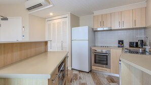 A modern kitchen with wooden cabinets, a white refrigerator, a stove, and a coffee maker. - The Pool Resort Kingscliff - 2B Ocean View (2320/21) - Holiday Management Co. (Tweed)