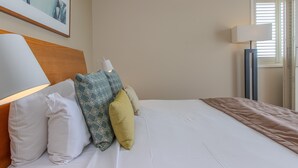 A neatly made bed with white bedding and multiple pillows, a modern lamp, and a framed picture on the wall. - The Pool Resort Kingscliff - 2B Ocean View (2320/21) - Holiday Management Co. (Tweed)