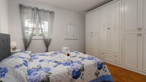 Ein Schlafzimmer mit Bett, Schrank, Nachttisch und Fenster mit Vorhängen.