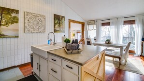 Une cuisine avec des meubles blancs, un plan de travail en bois et une fenêtre agrémentée de rideaux blancs.