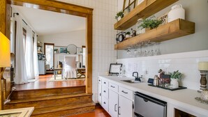 Une cuisine avec des armoires blanches, des étagères en bois et un plan de travail sur lequel se trouvent divers objets.