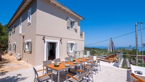 A two-story house with a balcony, a dining table set with plates and glasses, and a view of the sea.