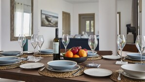 A dining table set with plates, glasses, a bottle of white wine, and a bowl of fruit.