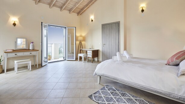 A bedroom with a bed, bedside tables, a desk, and a chair. There is a door leading to an outdoor area.