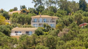 A two-story building with a tiled roof, surrounded by dense greenery and trees.