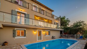 A two-story building with a swimming pool, outdoor seating, and a balcony with railings.