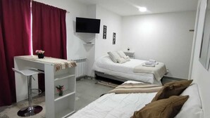 Makuuhuoneessa on sänky, työpöytä, tuoli, televisio ja ikkuna, jossa on verhot.