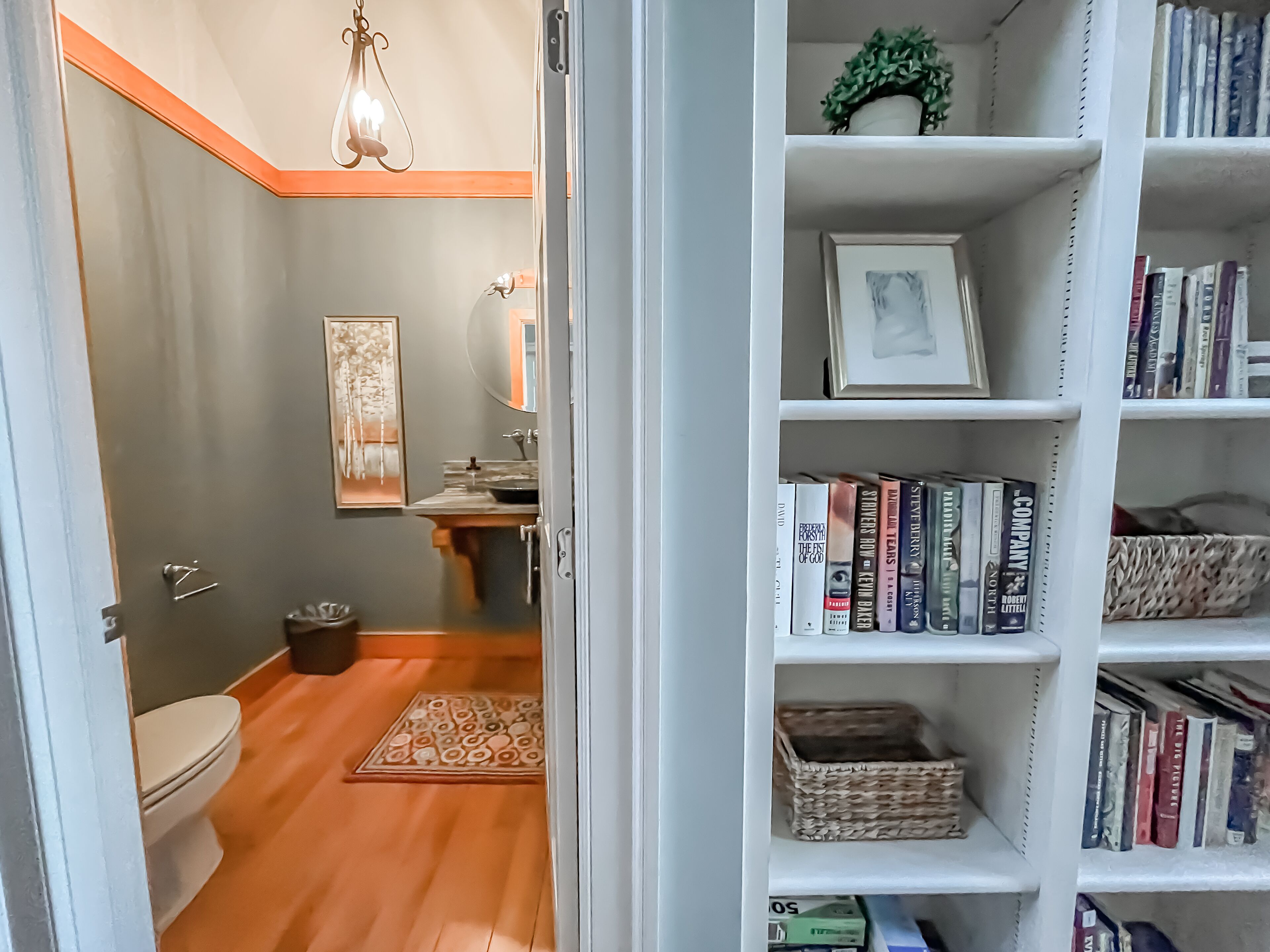 A bathroom with a toilet, sink, and mirror, and a bookshelf with books and decorative items.