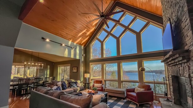 A spacious living room with a high ceiling, large windows, and a stone fireplace.