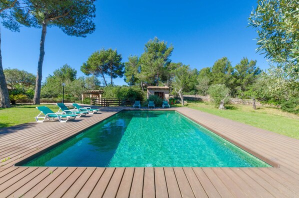 A rectangular swimming pool with clear water, surrounded by a wooden deck and green lounge chairs.
