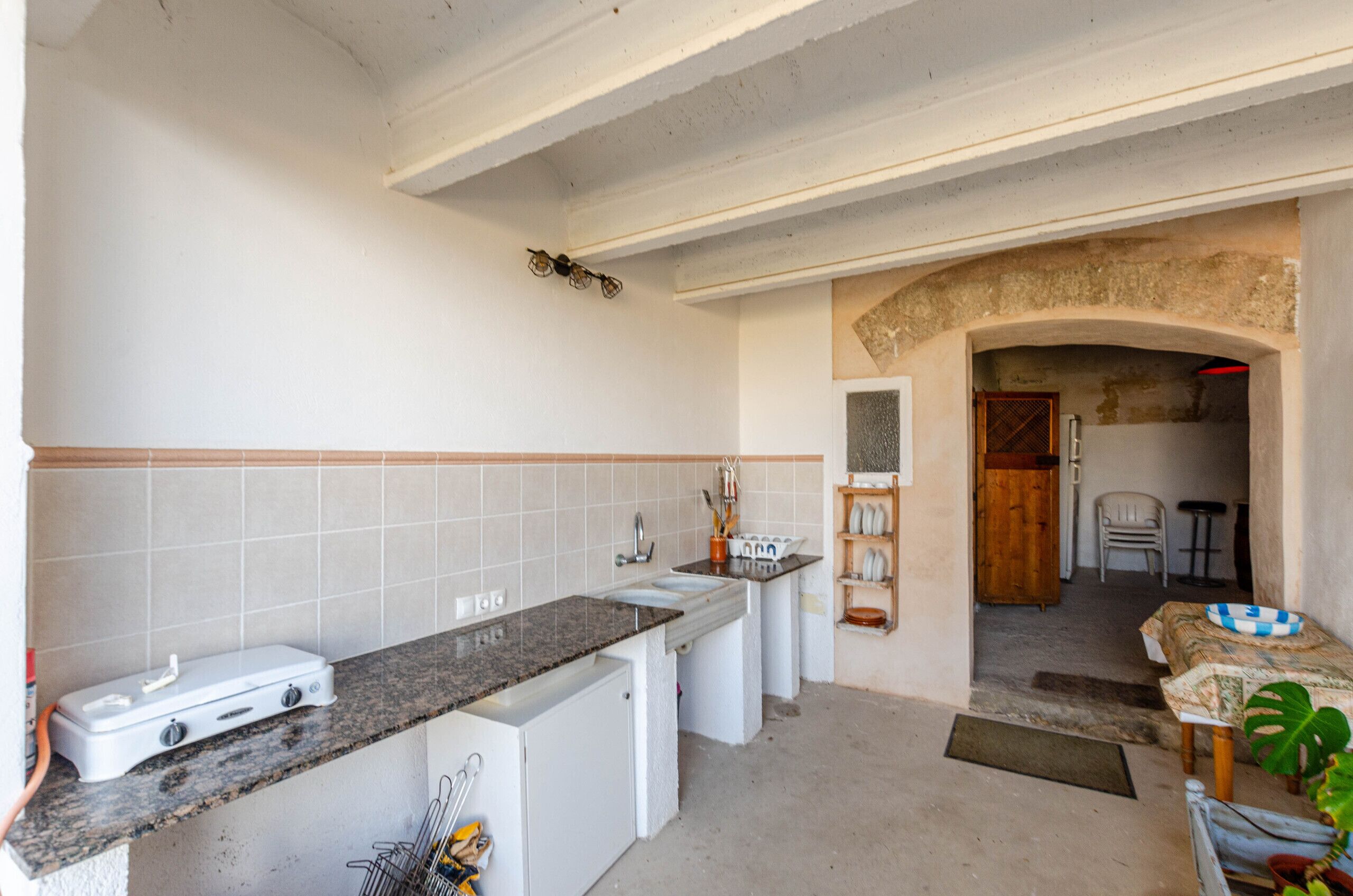 A compact kitchen with a built-in stove, a sink, and a countertop. There is a doorway leading to a dining area with a table and chairs.