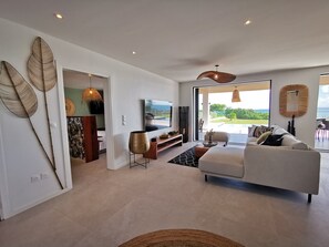A modern living room with a large sofa, a TV, and a dining area with a view of the outdoors. - On the beach, modern villa, swimming pool, panoramic sea view , tropical garden (Saint-François)