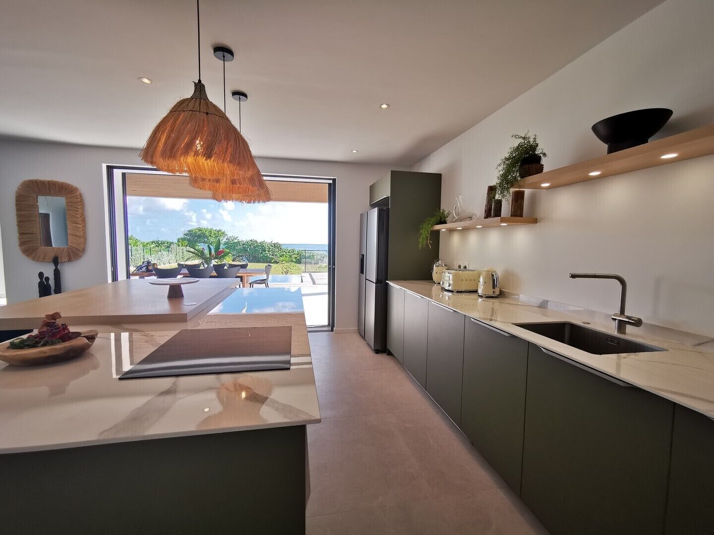 Une cuisine moderne dotée d’un grand îlot central, d’appareils électroménagers intégrés et offrant une vue sur l’extérieur.