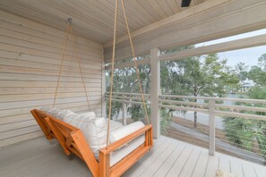 Une terrasse en bois avec un fauteuil suspendu et une vue sur le paysage environnant.