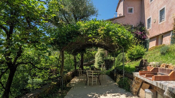 Un giardino con una pergola, un tavolo e sedie, e un edificio sullo sfondo.