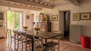 Una sala da pranzo rustica con un tavolo di legno, sedie bianche e pavimento piastrellato.