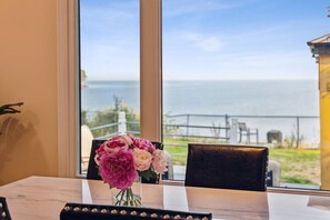 A dining table with a vase of flowers, a chair, and a view of the sea through large windows.