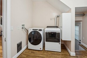 A laundry room with a front-loading washer and dryer, wooden flooring, and a white wall.