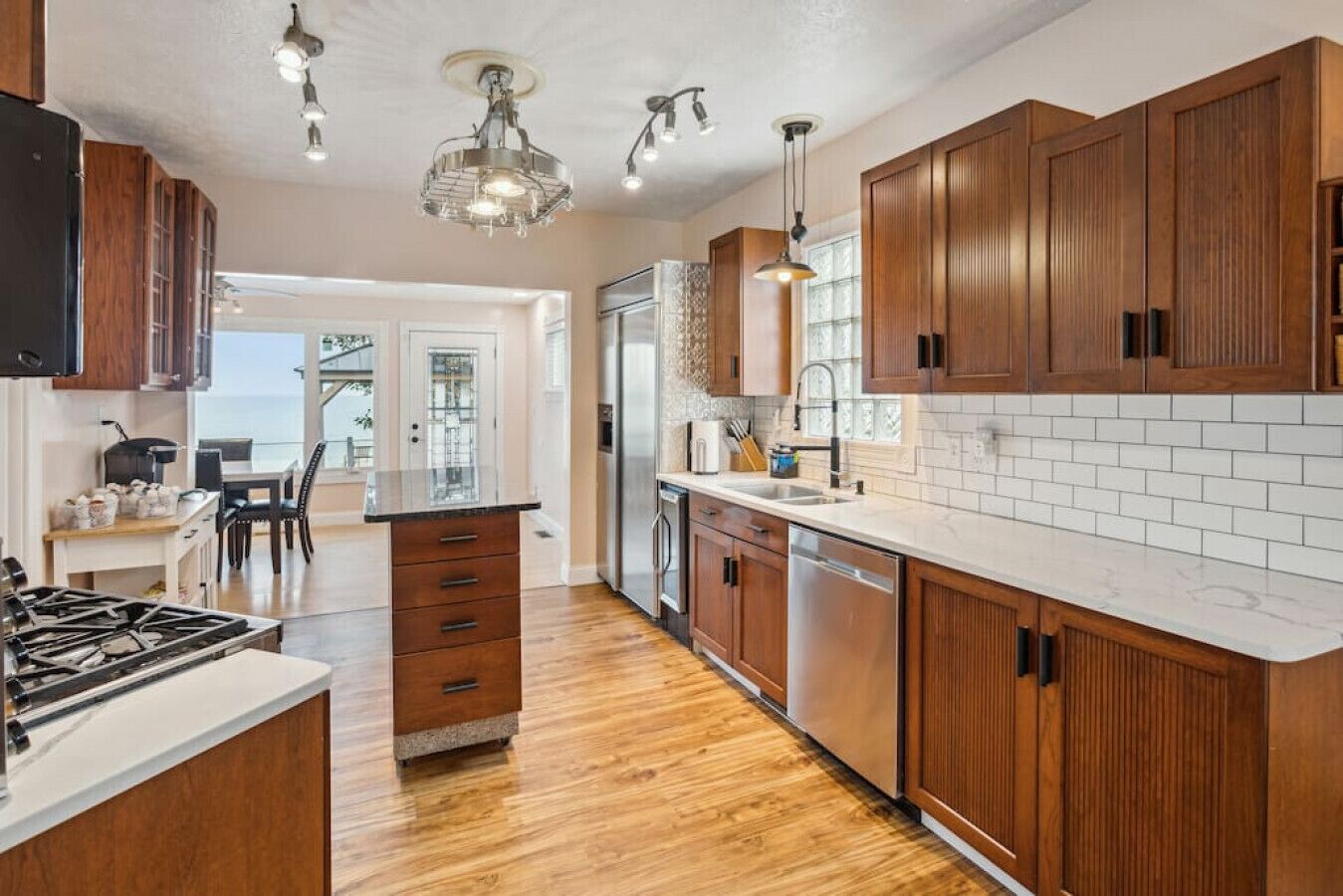 A modern kitchen with wooden cabinets, a central island, stainless steel appliances, and pendant lighting.