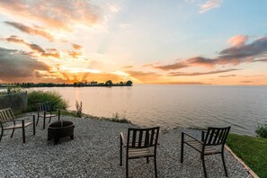 Eine Terrasse mit Sitzgelegenheiten im Freien und einem Feuerkorb mit Blick auf ein Gewässer bei Sonnenuntergang.