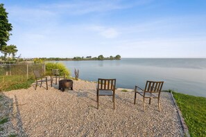 Un patio de grava con dos sillas de madera y un brasero, con vista a un lago tranquilo.