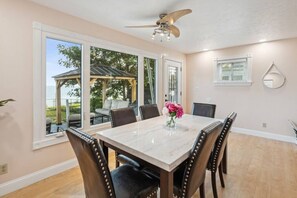 A dining area with a marble table, six chairs, a ceiling fan, and large windows offering a view of the outdoors. - Lakefront Retreat - Serene escape on Lake Erie! Amazing Views! Lorain OH (Lorain)