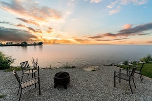 A lakeside seating area with chairs and a fire pit.