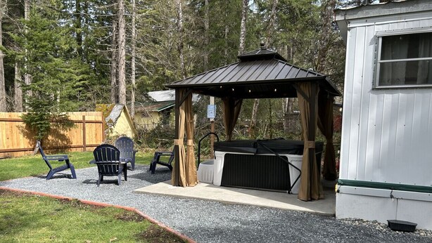 A covered outdoor seating area with a hot tub, two chairs, and a wooden pergola. - Retro Trailer - Hot Tub, AC, EV near Mt Rainier Nat`l Park in Ashford, WA (Ashford)