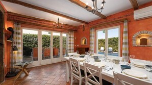 Un espace repas avec une grande table dressée pour le repas, des poutres en bois au plafond et une vue sur l’extérieur.