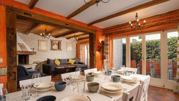 Un coin repas avec une table mise pour le repas, un canapé en arrière-plan et une vue sur l’extérieur grâce à de grandes portes vitrées.