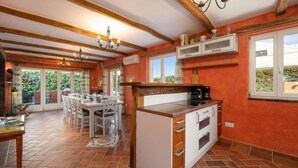 Une cuisine spacieuse avec un coin repas, comprenant un grand îlot central, des poutres en bois et une vue dégagée par les fenêtres.